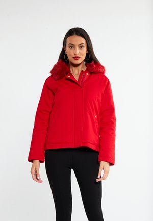 Rød pufferjakke med kunstpelskrave, lynlås lukning og sidelommer. Har et cropped design og tekstureret stof. Sorte leggings bæres under.