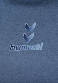 Modré bavlněné tričko s malým vypouklým logem "hummel" a dvěma vzory chevron nad ním, s texturovaným povrchem látky.