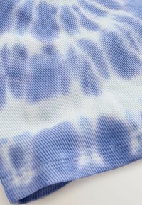 Tkanina s teksturom u plavoj i bijeloj boji s uzorkom tie-dye i rebrastim dizajnom. Vidljivo šivanje uz rub. Mekani, lagani materijal.