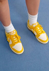 Kollane Nike'i jooksujalatsid valgete aktsentidega, millel on sile nahk, tekstuuriga samet ja auguline varvas, koos valgete sokkidega.