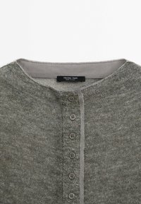 Harmaa nappikaulusneule, jossa on pyöreä pääntie ja näkyvä tuotemerkki etiketti sisäkauluksessa.