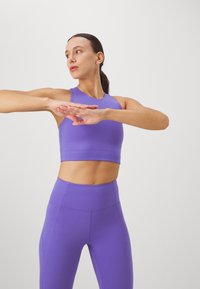 Violetti urheilullinen toppi ja korkeavyötäröiset leggingsit, valmistettu sileästä, venyvästä materiaalista. Suunnittelussa on klassinen hihaton leikkaus.
