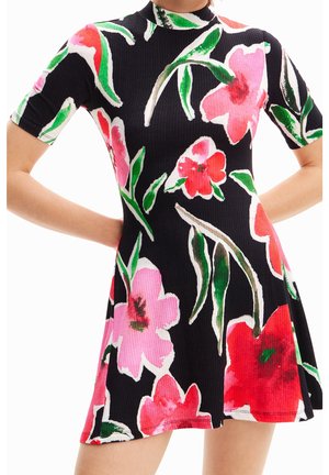 Schwarzes kurzärmeliges Kleid mit großem pink-rotem Blumenmuster, hohem Kragen und gerippter Struktur, getragen von einer Person mit Händen in der Hüfte.