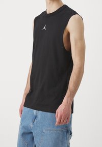 Svart ärmlös t-shirt i bomull med en liten vit logotyp på bröstet. Passformen är avslappnad och tyget är mjukt.