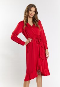 Rochie roșie, cu mâneci lungi și decolteu în V, cu un accent volan la margine și o curea la talie. Textură de țesătură netedă.