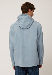 Chaqueta con capucha de color azul claro, fabricada en un tejido suave, con corte recto, puños elásticos y detalles en la costura trasera.