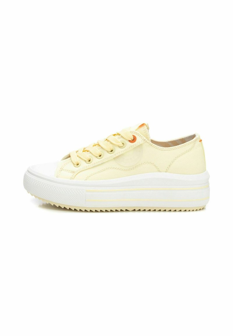 Zapatillas de lona amarillas con una suela de goma blanca, que presentan una entresuela gruesa, puntera redonda y agujeros para los cordones en color naranja. Suela texturizada para un mejor agarre.