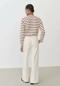 Brown and cream striped sweater, relaxed fit, paired with high-waisted white wide-leg pants. Smooth texture, minimalistic design, and two back pockets.