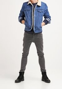 Veste en denim avec col en fausse fourrure, de couleur bleue, associée à un jean skinny gris et des bottes noires à lacets avec une semelle texturée.