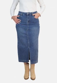 Falda midi de mezclilla en azul medio con una abertura frontal, cintura alta, presillas para cinturón y bolsillos. Combinada con botas de tobillo beige.