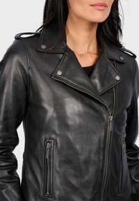 Černá kožená motocyklová bunda s stříbrnými prvky, se zipovými kapsami a širokými klopami, která vystihuje hladkou strukturu a přizpůsobený střih.