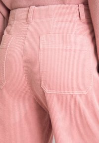 Różowe sztruksowe spodnie w paski pionowe, z wysokim stanem i dwoma tylnymi kieszeniami. Materiał ma miękką fakturę.