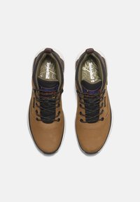 Zapatillas de cuero marrón con detalles de malla negra, cordones redondos y un collar acolchado. Plantilla texturizada con la marca Timberland visible.