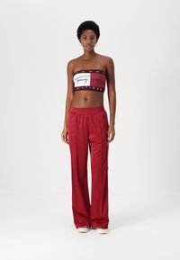 Sarkans croptops ar baltu logo, apvienots ar brīvā griezuma augstvērtīgām sarkanām satīna biksēm. Gluda tekstūra un brīvs piegriezums.