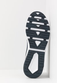 Sport shoe with a textured black rubber sole featuring a white midsole, distinct tread patterns, and a branding logo on the heel.