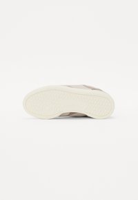 Beige sneaker with a textured rubber sole, smooth upper, and subtle tonal accents. Features a minimal design with no visible branding.