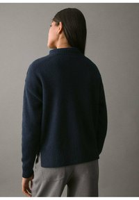 Granatowy sweter z dzianiny z wysokim kołnierzem, ściągaczami przy mankietach i u dołu, o luźnym kroju i fakturowanym wykończeniu. Minimalistyczny design.
