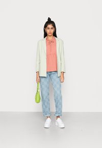 Blazer verde menta, blusa coral com babados, jeans claros xadrez, ténis brancos de plataforma, segurando uma pequena mala verde-lima.