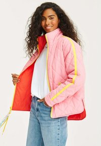 Prošívaná bunda v růžové barvě s kontrastním červeným interiérem. Má žluté akcenty a vysoký límec. Přední zip a postranní kapsy.