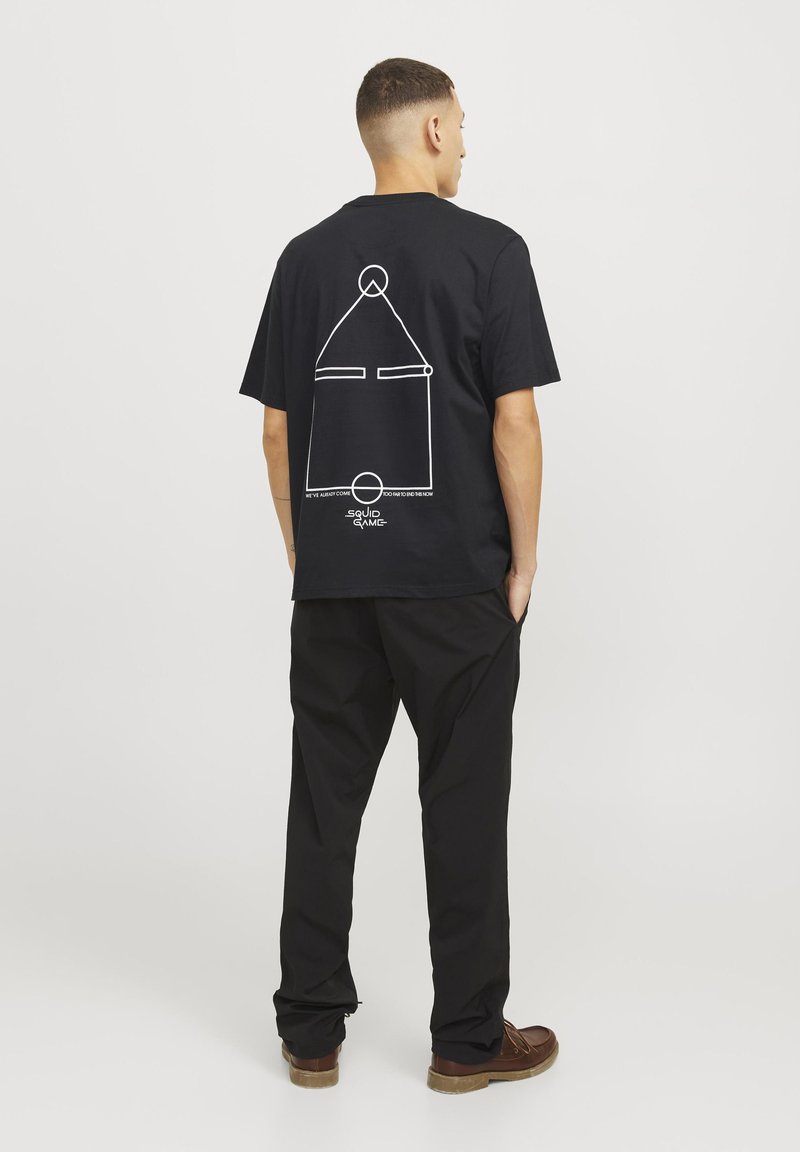 Sort bomulds T-shirt med et hvidt geometrisk design på ryggen, samt teksten "SQUID GAME" og yderligere sætninger nedenfor.
