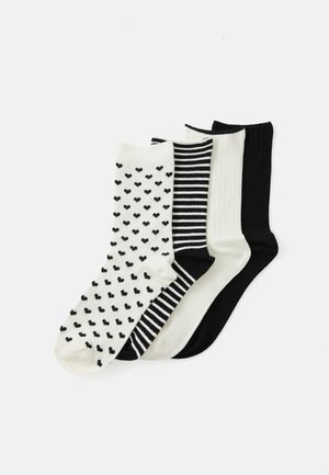 Trois paires de chaussettes : une avec de petits cœurs noirs sur fond blanc, une rayée noir et blanc, une complètement noire, et une complètement blanche avec une texture côtelée.