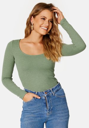 Top a maniche lunghe in tessuto ribbed di colore verde salvia, con scollatura a barca. Abbinato a jeans in denim blu a vita alta, che mettono in risalto una silhouette aderente.