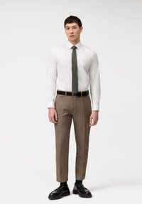 Weißes Langarmhemd, dunkelgrüne Krawatte, beige Hose, schwarzer Gürtel und schwarze Schuhe. Glattes Material, taillierte Passform, maßgeschneiderte Silhouette.