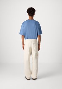 Camiseta de manga corta azul claro y pantalones cargo color crema con bolsillos laterales, con un discreto parche de logo rojo en la parte posterior.