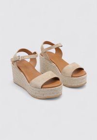 Sandalias de cuña beige con parte superior de tela texturizada, punta abierta, tira al tobillo con hebilla y suela de plataforma de yute trenzado.