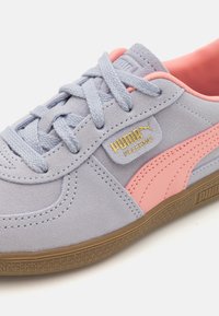 Svijetloplave suede tenisice s ružičastim akcentima i sivim vezicama. Imaju zlatnu oznaku s logotipom i strukturiranu smeđu gumenu petu.