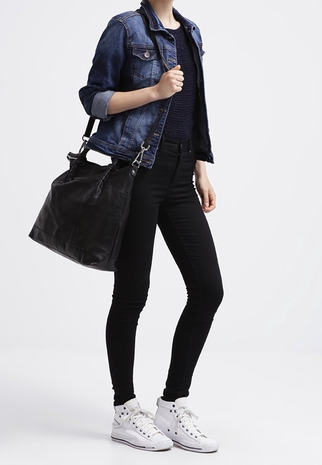 Personne portant une veste en jean bleue, un pantalon noir, des baskets montantes blanches, avec un grand sac à main en cuir noir sur l'épaule.