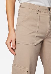 Beige Cargo-Hosen aus Baumwollmischung mit Seitentaschen und geradem Schnitt. Der Stoff hat eine glatte Textur mit sichtbaren Nähten.
