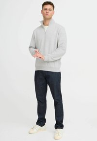Grijze zip-up sweatshirt met een hoge kraag, zacht materiaal, geribde manchetten, gecombineerd met donkerblauwe jeans en witte sneakers.
