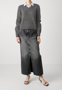 Grijze wollen trui met lange pofmouwen en een V-hals, gecombineerd met een donkere denim maxi rok met een voorste split. Zwarte sandalen met een kleine hak.