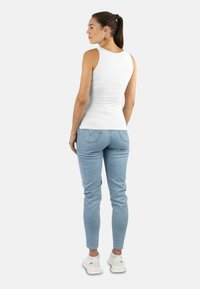 Weißes ärmelloses Oberteil mit figurschmeichelndem Design, kombiniert mit hellblauen Skinny-Jeans, die eine glatte Textur und eine schlichte Silhouette zeigen.