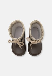 Bottes en caoutchouc marron avec une tige beige, col roulé et lacets bruns noués. Texture lisse avec une semelle robuste et un design minimaliste.