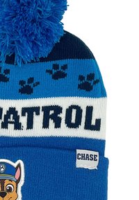 Blauwe gebreide muts met een fluffy pompon, voorzien van pootafdrukken en de tekst "Paw Patrol" in het wit, met een label met de tekst "Chase" aan de zijkant.