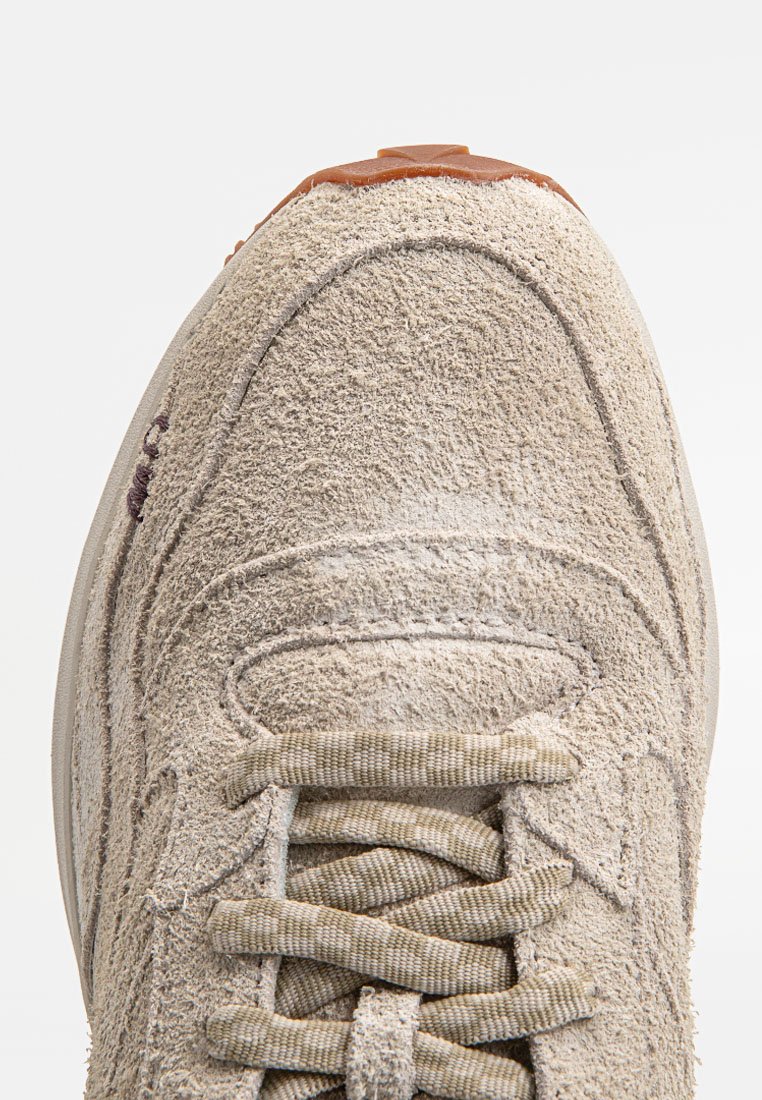 Sneaker in suede beige con superficie testurizzata, punta rotonda, lacci beige e suola in gomma marrone. Presenta cuciture tono su tono e un colletto imbottito.