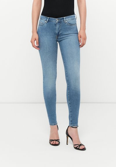 Jeans skinny en denim bleu clair avec une coupe ajustée, style cinq poches et une légère décoloration. Associés à des sandales noires à talons hauts.