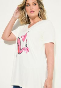 Vit t-shirt med kort ärm som har en grafisk design av en rosa högklackad sko, en martiniglas, läppstift och en blomma. Mjukt tyg med en avslappnad passform.