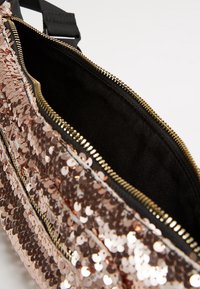 Fanny pack aperto in paillettes rosa oro con zip dorata e rivestimento interno in tessuto nero, con la zip superiore parzialmente aperta.