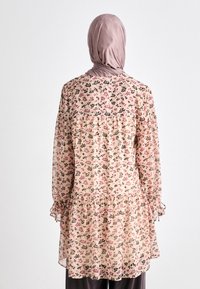 Lett, blomstermønstret tunika i myk ferskenfarge med svarte og lilla detaljer. Har lange ermer og en tiered, volang nederkant.