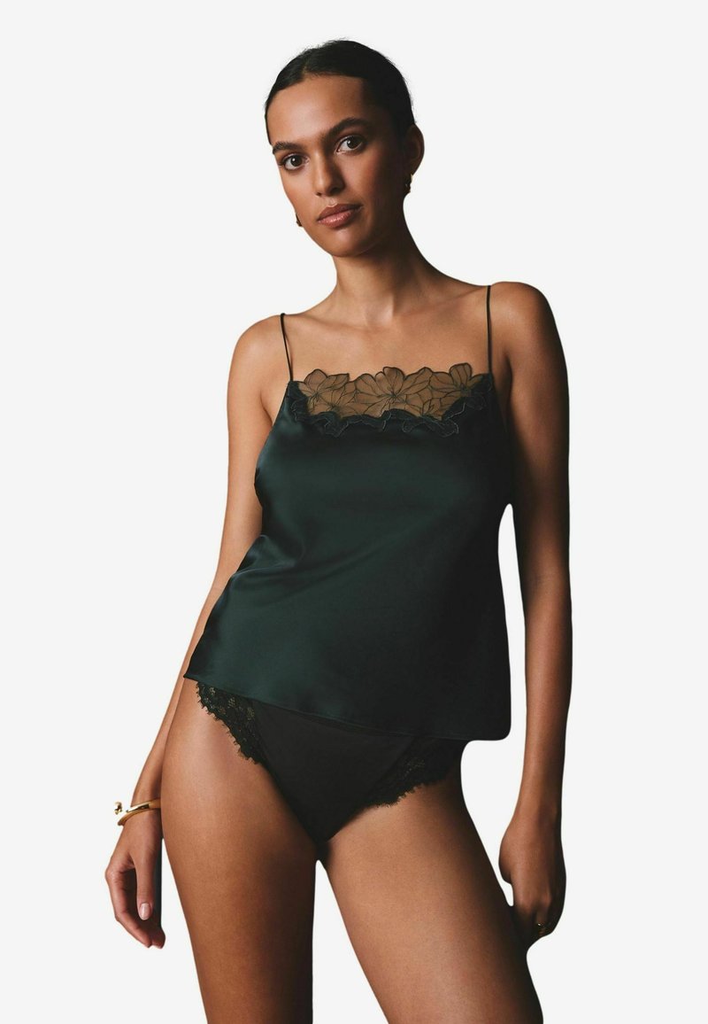 Schwarze Satin-Camisole mit durchscheinendem floralen Spitzenbesatz am Ausschnitt, dünnen Spaghetti-Trägern, kombiniert mit schwarzen Spitzenbesatz-Panties. Sanfte Textur.