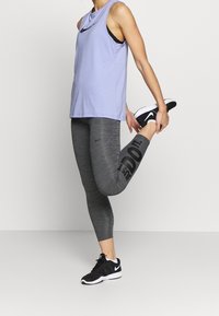 Top atletico senza maniche di colore viola chiaro abbinato a leggings grigi con il testo nero "JUST DO IT", completato da scarpe da ginnastica nere.