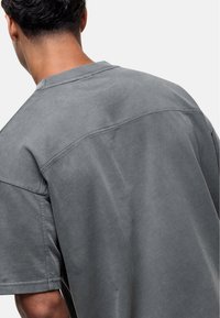 Grijze oversized t-shirt van katoen, met een ronde hals, korte mouwen en een rugpas detail. Gladde textuur met gestikte accenten.
