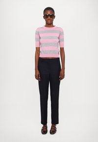 Grå og rosa stripete kortermet genser med cropped design. Kombinert med mørke bukser og svarte solbriller, foran en ensfarget bakgrunn.