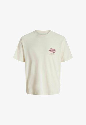 Kermansävyinen puuvillapaita, jossa on pyöreä kaula-aukko ja lyhyet hihat. Rinnan alueella on punainen painettu logo, jonka alla on lisätietoa.