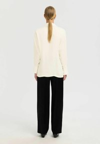 Cremfarbener Langarmshirt mit rundem Halsausschnitt, kombiniert mit hoch taillierten, schwarzen weiten Hosen. Glatter Stoff, lockere Passform und minimale Nähte.