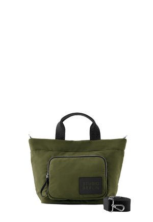 Olivgrüne Tragetasche mit schwarzen Griffen, vorderer Reißverschlusstasche mit der Aufschrift „Studio Berlin“ und separatem schwarzen verstellbaren Tragegurt.