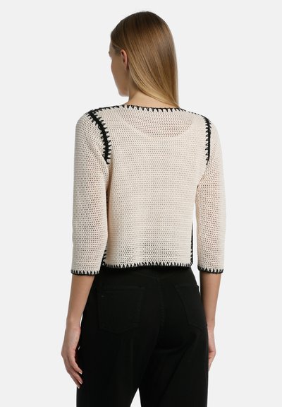 Beige neulepaita, jossa on mustat reunat, kolmivartiset hihansuut ja lyhyt malli. Ominaisuuksina teksturoitu, avonainen kudonta.